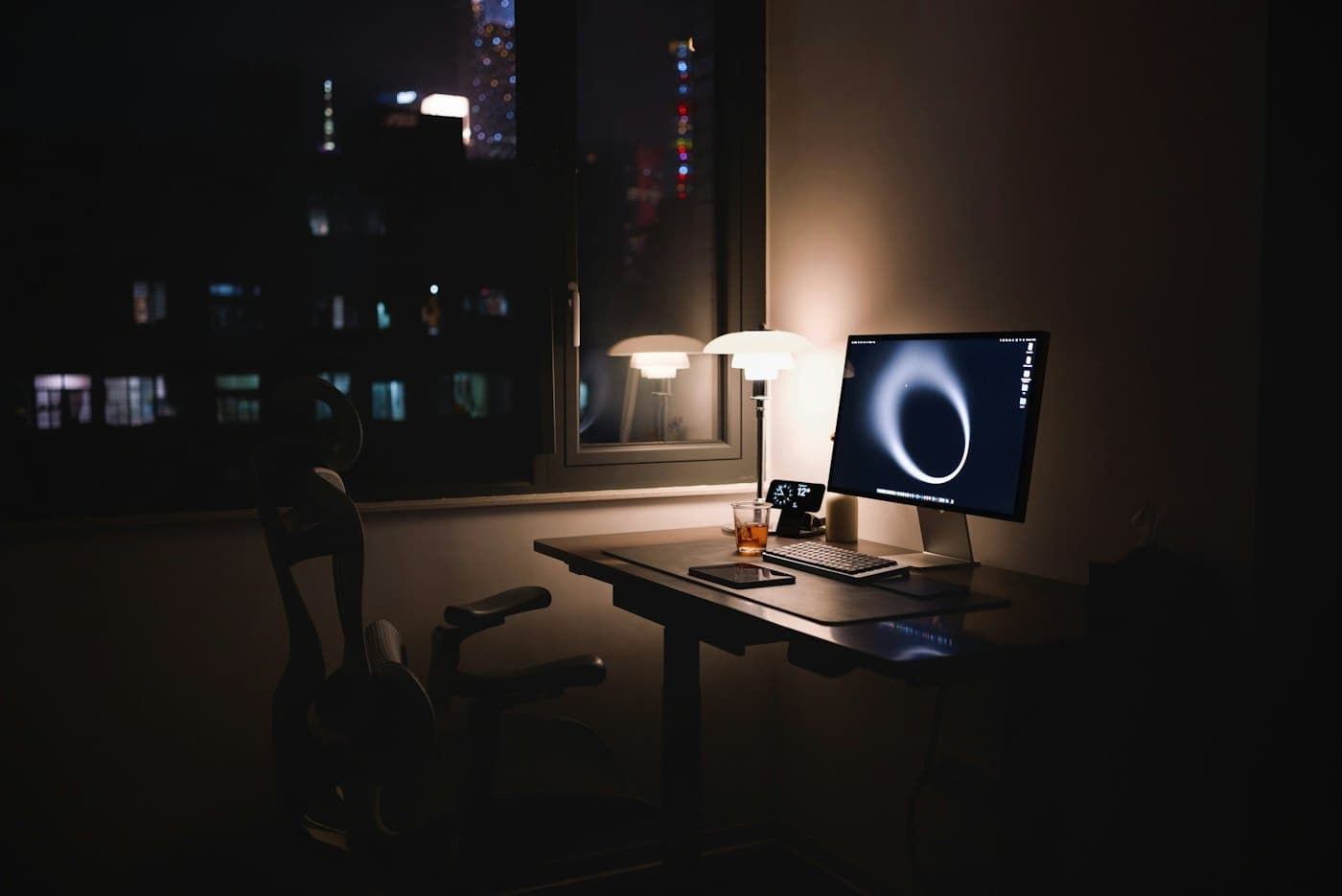 Empty desk at night with the monitor still on and the chair pushed in